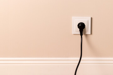White european electrical outlet with black plug inserted into it on modern beige wall