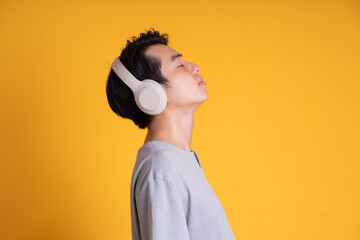 image of asian man listening to music with headphones, isolated on yellow background