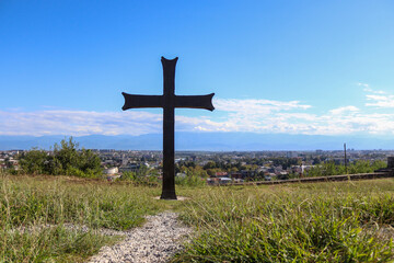 Fototapeta na wymiar Cross on the hill with Georgian city landscape on background