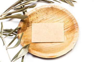 Plato redondo de madera con tarjeta sen blanco junto a unas ramitas de olivo sobre un fndo blanco. Vista superior y de cerca. Copy space - obrazy, fototapety, plakaty