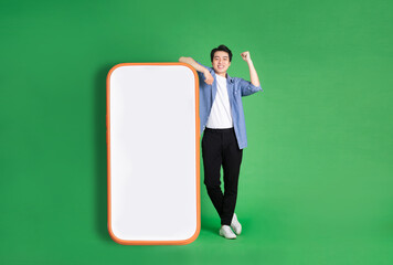 full body image of asian man standing next to big smartphone, isolated on blue background