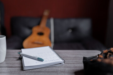 A notebook with music chords is resting on a table with a Mexican jarana guitar in the background