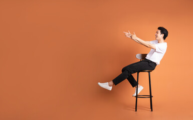 image of asian man sitting on a stool, isolated on orange background