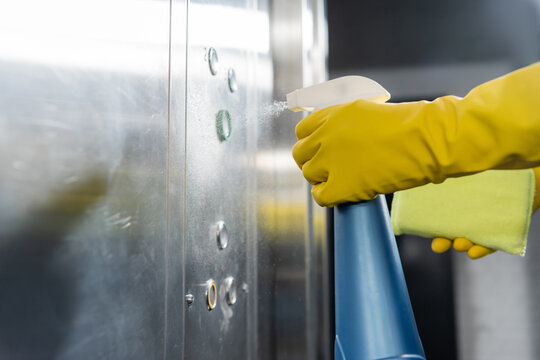 partial view of cleaner spraying detergent while washing office elevator.