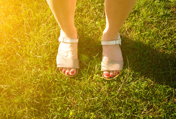 Woman feet in sandals stand in the green grass. Sunny summer day. Relax and travel concept.