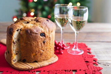 Fototapeta na wymiar Panettone and wine glasses on wooden table with Christmas decorations and tree in the background.
