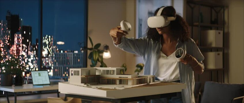 Portrait of African American female architect or student using a virtual reality VR headset to work on a house project late at night, preparing for presentation with a client