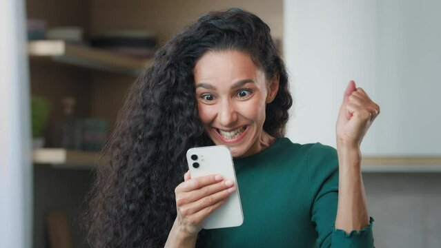 Amazed excited shocked woman joyful champion buyer reads positive notification on mobile phone feels euphoria emotion wow reaction wins online bet black friday sales internet lottery surprise victory