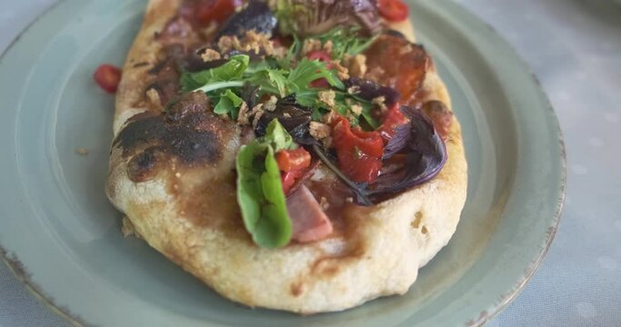 Camera fly over an oval small pizza with paperoni lying on a plate in a restaurant. Close-up, delicious Italian food.