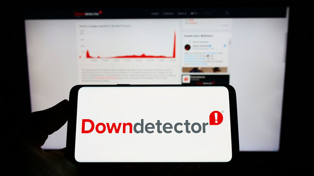 Stuttgart, Germany - 09-08-2022: Person holding mobile phone with logo of online platform Downdetector (Ookla LLC) on screen in front of web page. Focus on phone display.