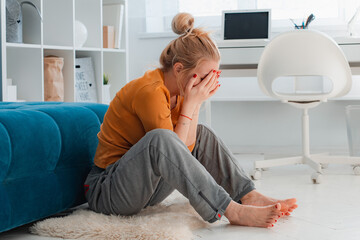 Unhappy woman depressed touching hair, sitting on floor at home, thinking about problems, upset girl feeling lonely and sad, psychological and mental troubles