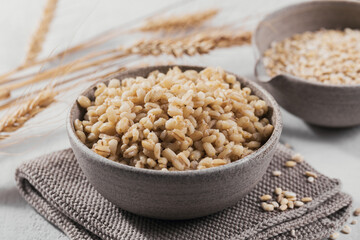 Bowl of cooked peeled barley grains porridge with ears of wheat on white background. Cooking Healthy and diet food concept.