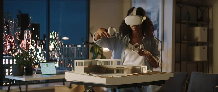 Portrait of African American female architect or student using a virtual reality VR headset to work on a house project late at night, preparing for presentation with a client
