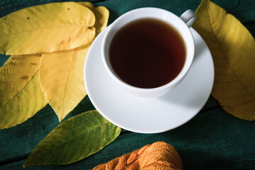 Top view of white ceramic cup of tea on green background with yellow autumn fall leaves