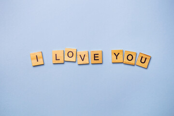 Inscription I love you in wooden square letters on a light blue background. Ready postcard, banner, place for an inscription.