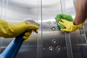Fototapeta na wymiar partial view of cleaner in rubber gloves holding detergent and cleaning buttons in elevator.