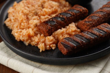 Traditional south european skinless sausages cevapcici made of ground meat and spices on black plate on dark wooden board, vegan substitute made of soy protein, with rice and sour cream
