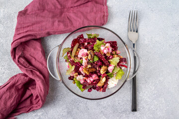 beetroot salad, green leaves, feta cheese, walnuts in a glass plate, a burgundy napkin and fork lie on a gray table
