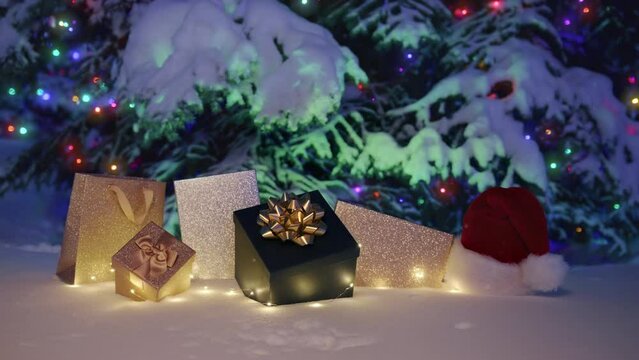 Magic snowfall on Merry Christmas eve magic winter night. Happy New Year 2023 night, golden gift boxes and present bags, colorful light garland on snowy tree blurry background. RED camera 6K footage