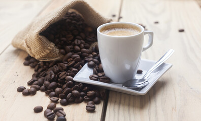 Taza de cafe caliente junto a un saco de tela con granos de café