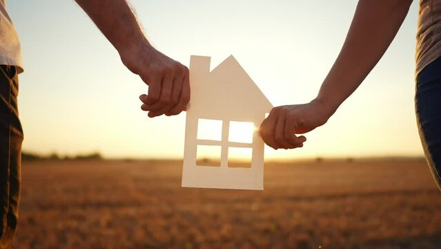 paper house happy family. friendly family hands holding paper house the glare of the sun shine through the window a beautiful sunset. mortgage business construction concept lifestyle. house dreams