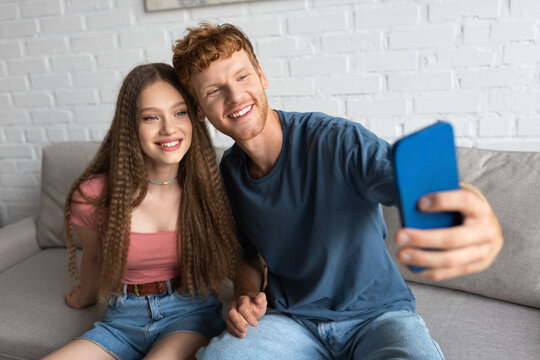 young redhead man taking selfie with happy girlfriend in living room.