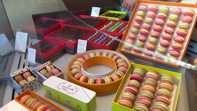 Life in the Confectionery Makarunov Pierre Edme in white sellers fuss trying to please buyersA lot of macaroons and a girl in white chooses a taste 06.04.22 Paris France. High quality 4k footage