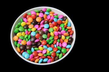 Colorful sugar coated chocolate candies in wooden bowl on white background with space for text, selective focus, top view.
