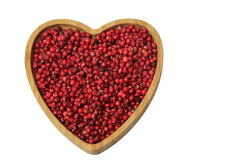 Pink pepper berries (Schinus terbinthifolia) in heart-shaped wooden bowl isolated on white background, top view.