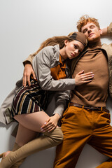 top view of stylish young man and girl in autumnal outfits lying together on grey.