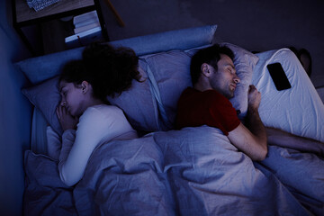 Fototapeta na wymiar High angle view of young couple sleeping under blanket in bed at night