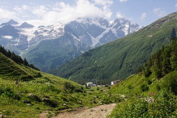 Panoramic view of the village of Terskol with residential buildings among the high slopes of mountains with glaciers on the tops on a sunny summer day in the Elbrus region in the North Caucasus