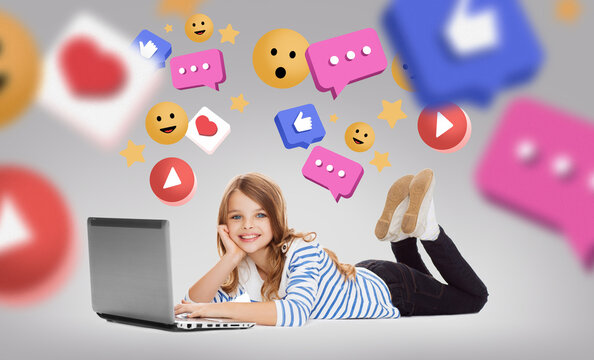 social media, technology and blogging concept - smiling little student girl with laptop computer lying on floor with internet icons over grey background