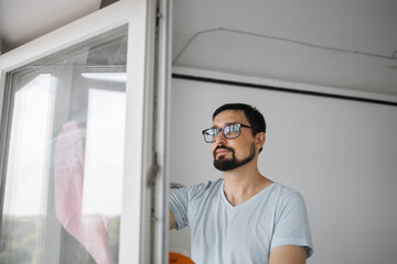 Close up portrait of bearded caucasian man in eyeglasses, sitting on stepladder holding sponge for washing windows and detergents, cleaning the apartment after renovation is completed.