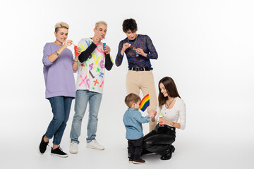 young lgbtq community friends blowing soap bubbles near toddler boy on grey background.