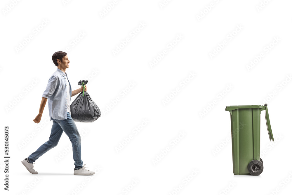 Sticker Full length profile shot of a casual young man walking towards a bin and carrying a plastic garbage bag