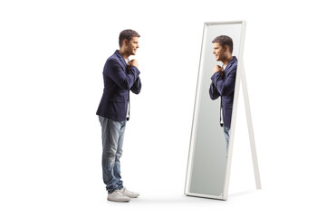 Full length profile shot of a young man getting ready and looking at a mirror - obrazy, fototapety, plakaty