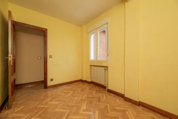 Empty room with an aluminum window, radiator in a niche, varnished oak parquet flooring and wooden doors