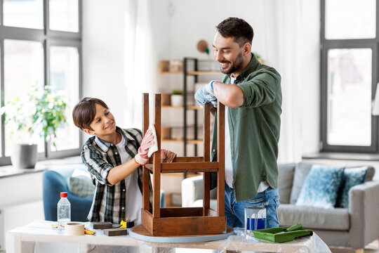 renovation, diy and home improvement concept - happy smiling father and son degreasing old round wooden table surface with tissue