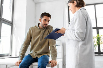 Obraz premium medicine, healthcare and people concept - female doctor with clipboard and male patient having health problem at hospital