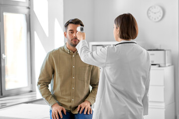 medicine, healthcare and people concept - female doctor with infrared forehead thermometer...