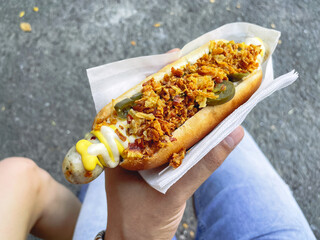 Man holds a hot dog with fried onions and peppers in his hand. Selective focus. Street food