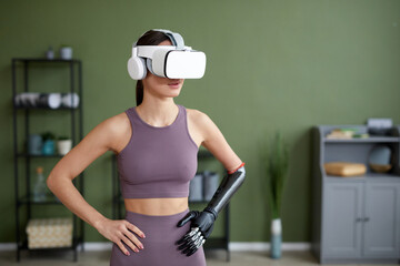 Young woman with prosthetic arm doing exercises in VR glasses in the room - obrazy, fototapety, plakaty