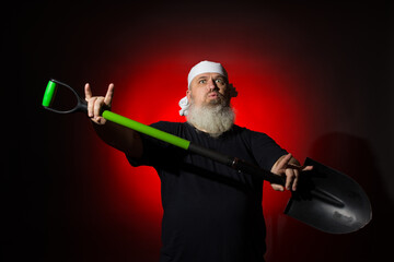 a strange man with a beard with a bandage on his head dances with a shovel to rock music on a red...