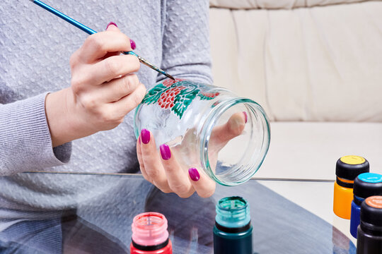 A girl paints a glass jar with stained glass paints
