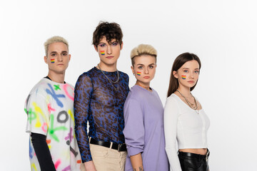 Obraz premium young and stylish people of different identity and with rainbow flags on faces looking at camera isolated on grey.