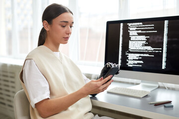 Young woman with disability using her smartphone at work while sitting at table with computer