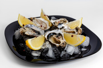 Oysters with lemon. Served black plate. White background.
