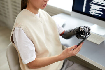 Close-up of young girl with prosthetic arm typing codes on smartphone while working at her...