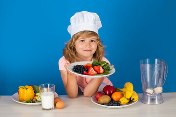 Cooking children. Chef kid boy hold plate with fruits making fresh vegetables for healthy eat. Portrait of little child in form of cook isolated on grey background. Kid chef. Cooking process.